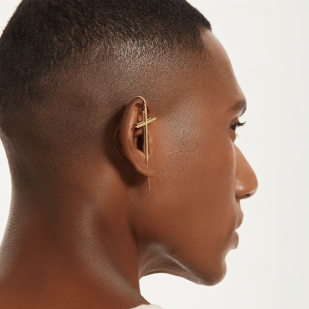 Cross ear cuff in gold worn on the ear, profile view